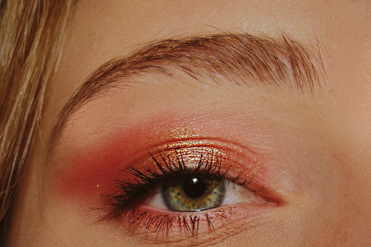Gros plan sur un œil maquillé de rose cuivré et de doré, cils recourbés