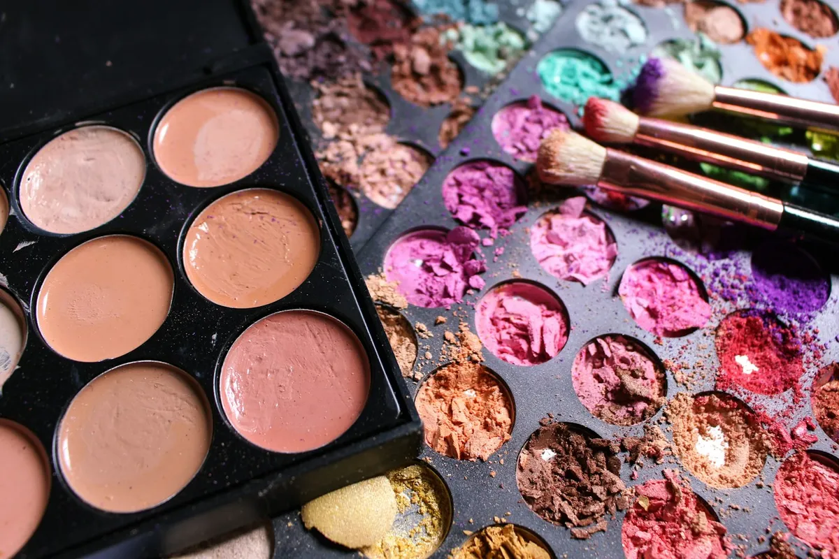 Palette de fards et correcteurs aux teintes pêche, avec pinceaux posés dessus